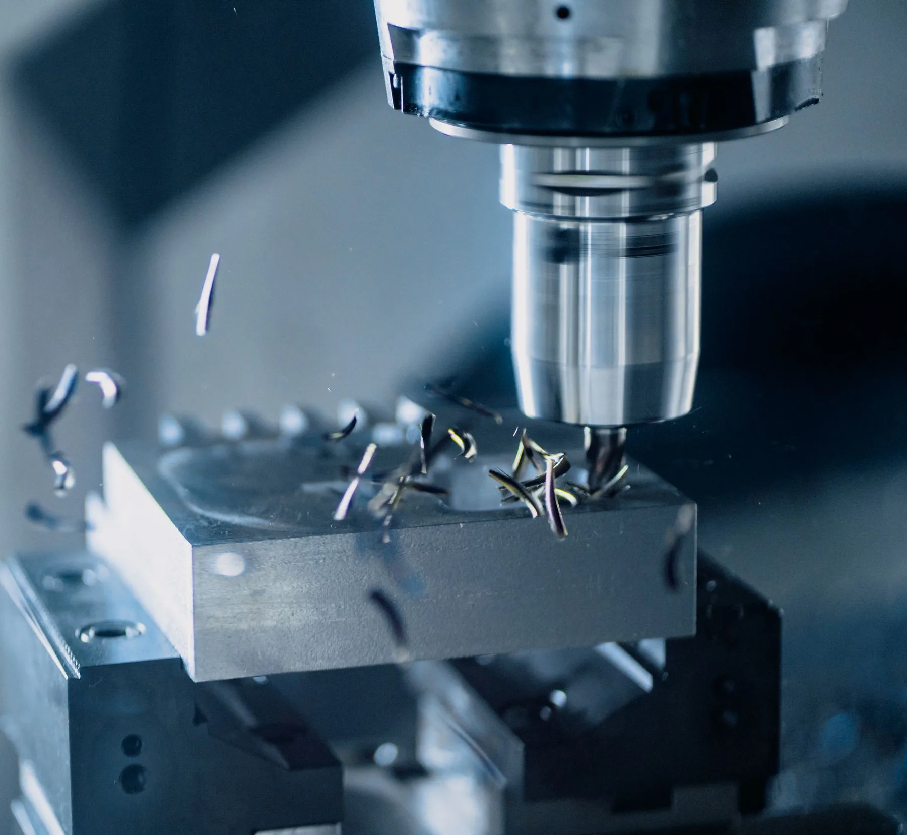 CNC milling cutter machining a metal block with freshly cut chips around the tool.