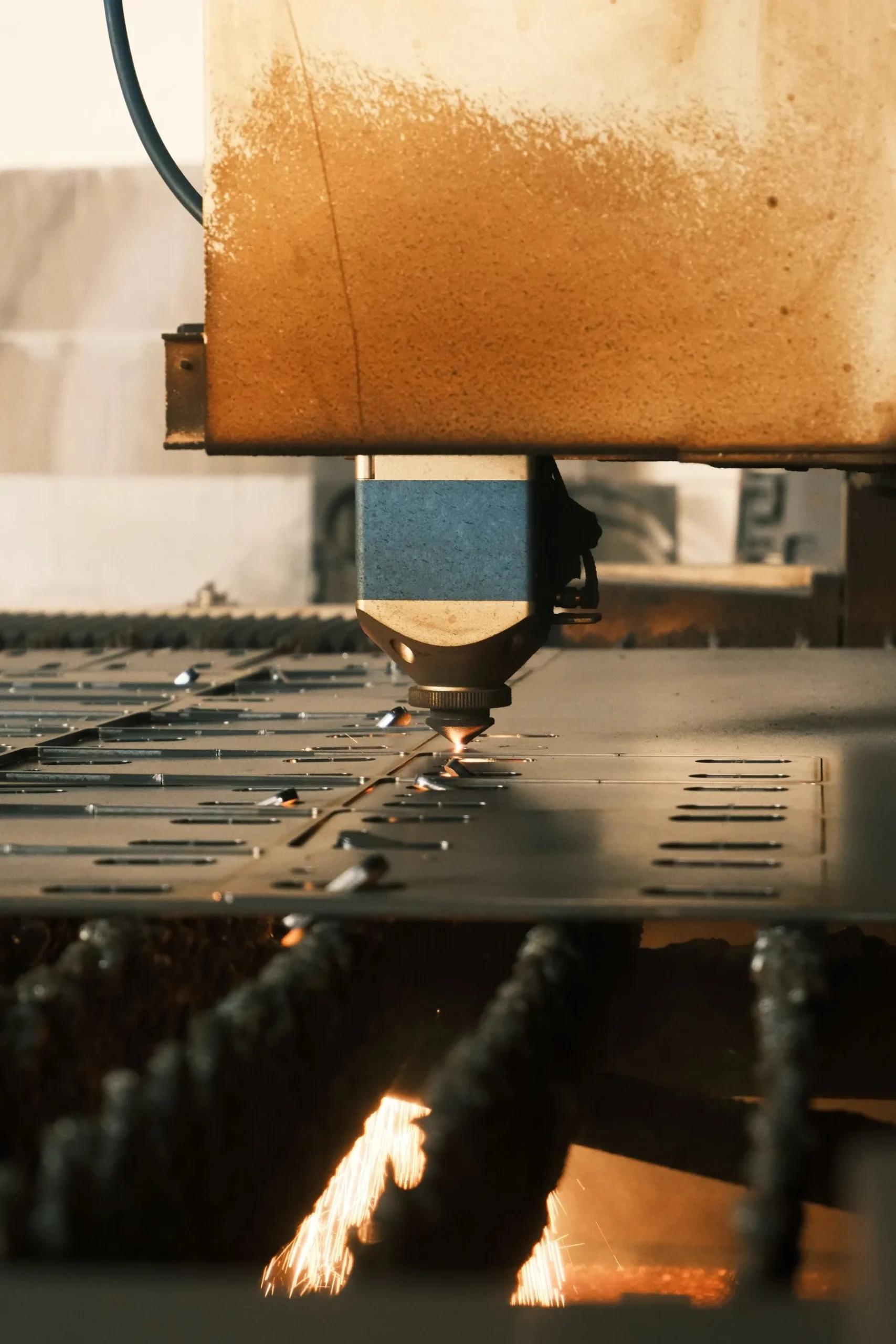 Industrial laser cutting head processing a perforated sheet-metal panel.