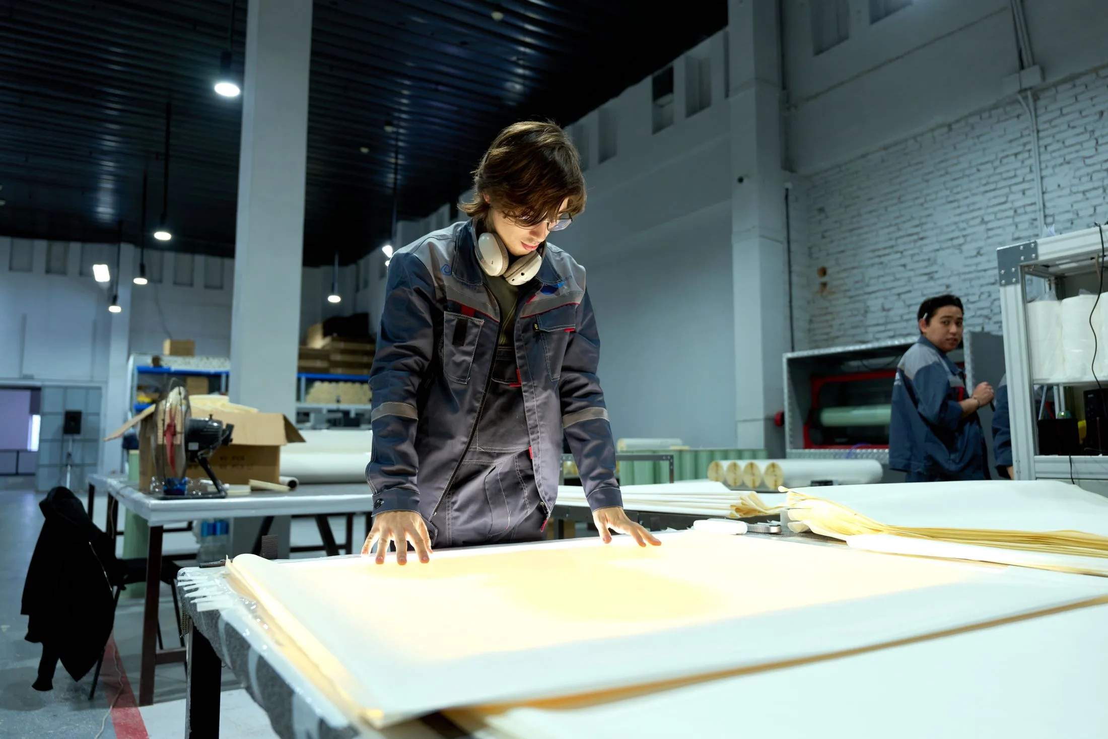 Manufacturing worker inspecting sheet material on a large worktable in a production facility.